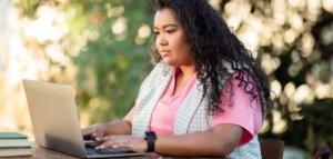 Plus size brown skinned feminine person with long black hair, pink shirt searches for a therapist on her laptop