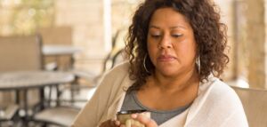 Black woman looking contemplative and serious, holding a mug, wearing a sweater with a nondescript background.